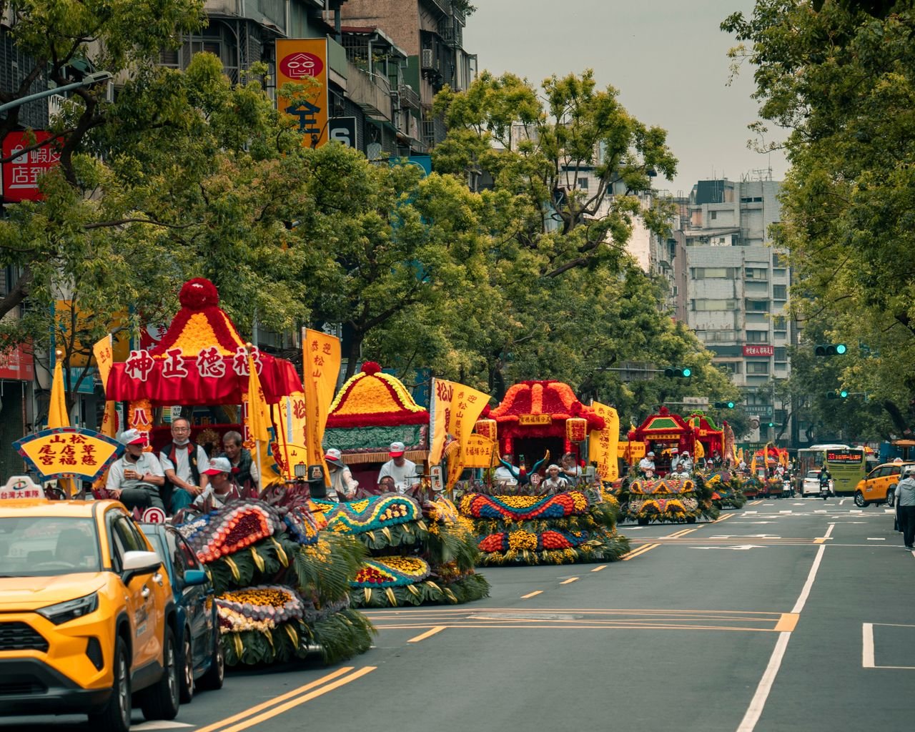 Colorful parade floats and vibrant displays line a lively urban street full of spectators.