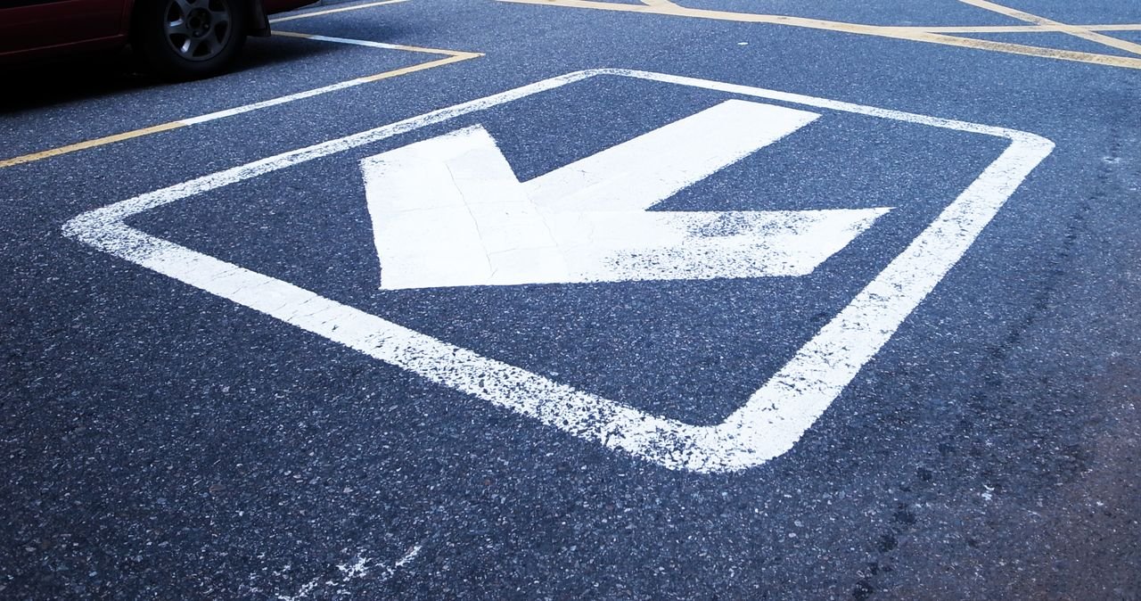 Close-up shot of a white arrow painted on asphalt indicating direction.